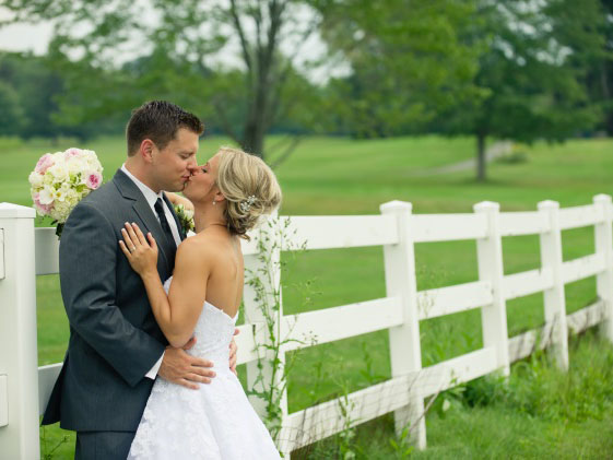 bride and groom kissing by white fence
